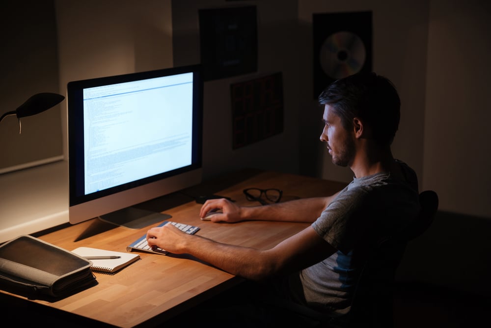 Handsome young man sitting in dark room and using computer-1